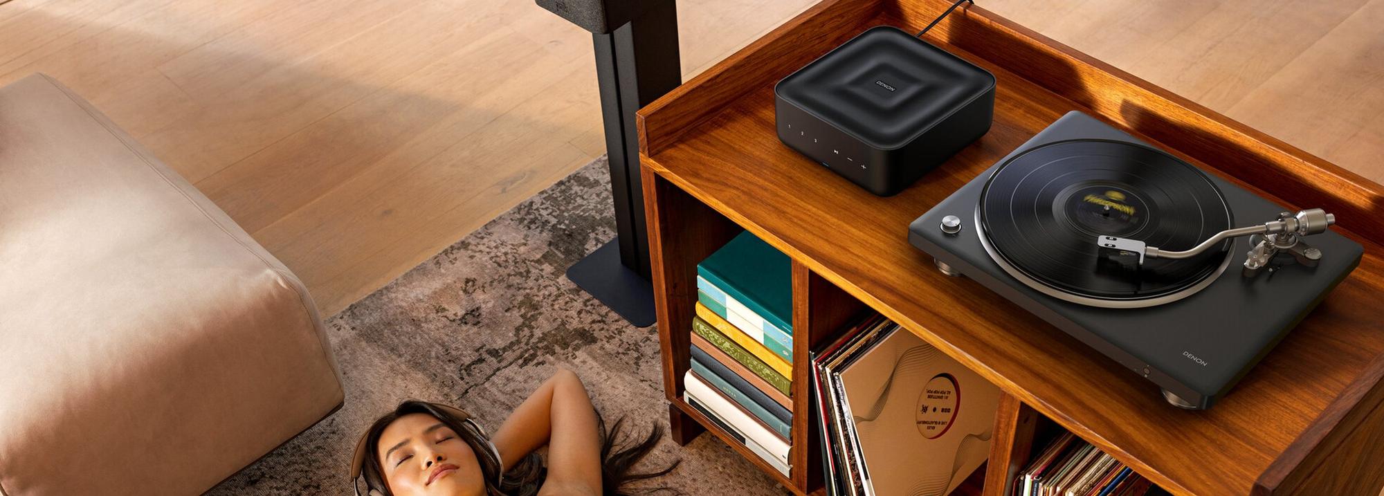 Denon turntable on a cabinet beside a record collection in a sunlit living room